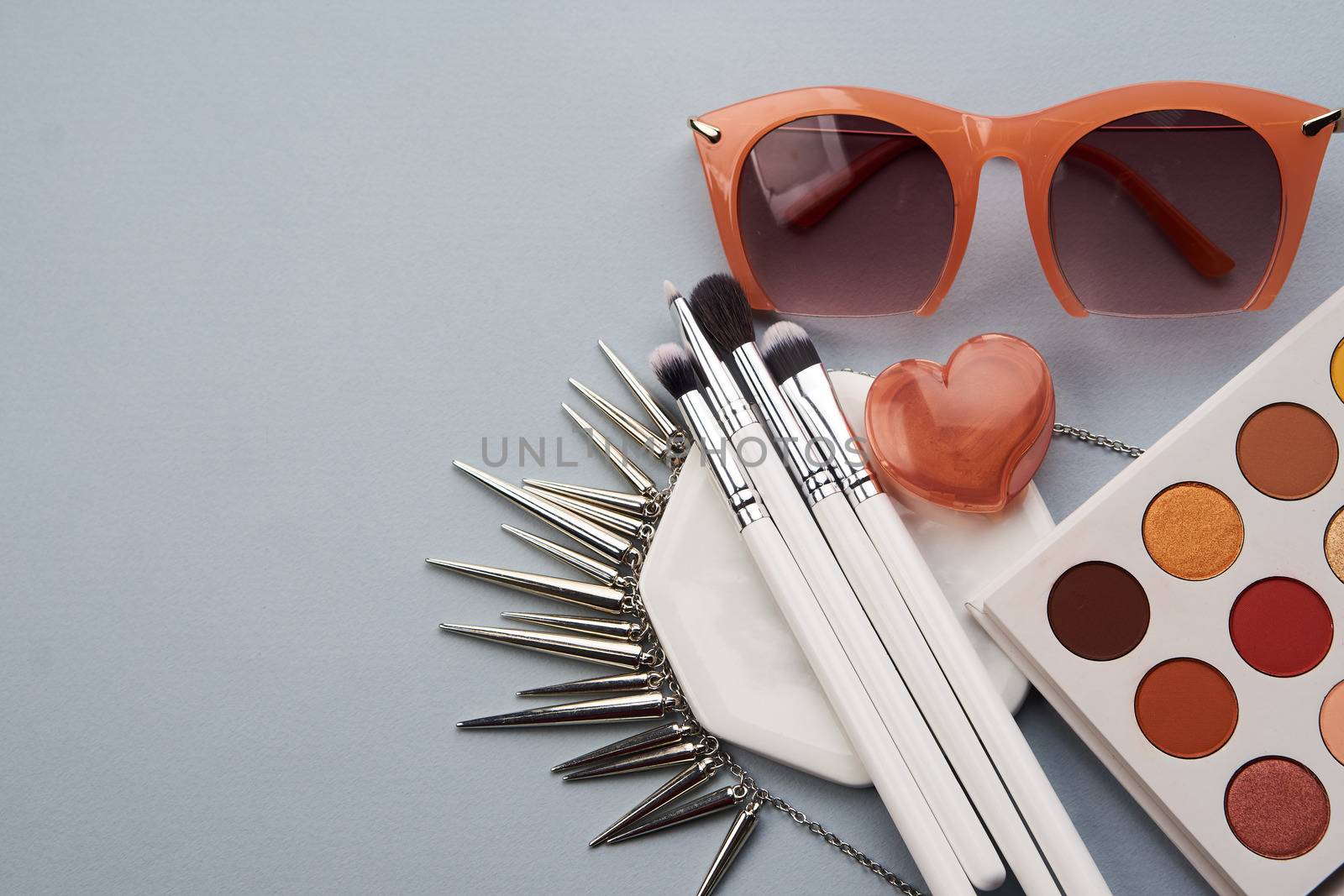 Professional cosmetics fashionable glasses on a stand on a gray background and makeup brushes top view by SHOTPRIME