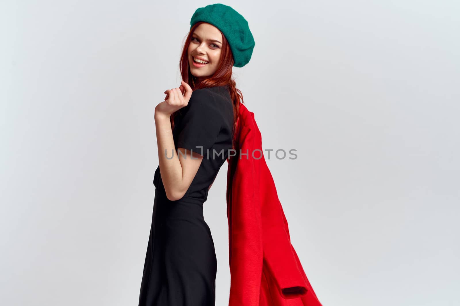 A woman holds in her hand a red coat and a dark T-shirt Green hat cropped view of a light background. High quality photo