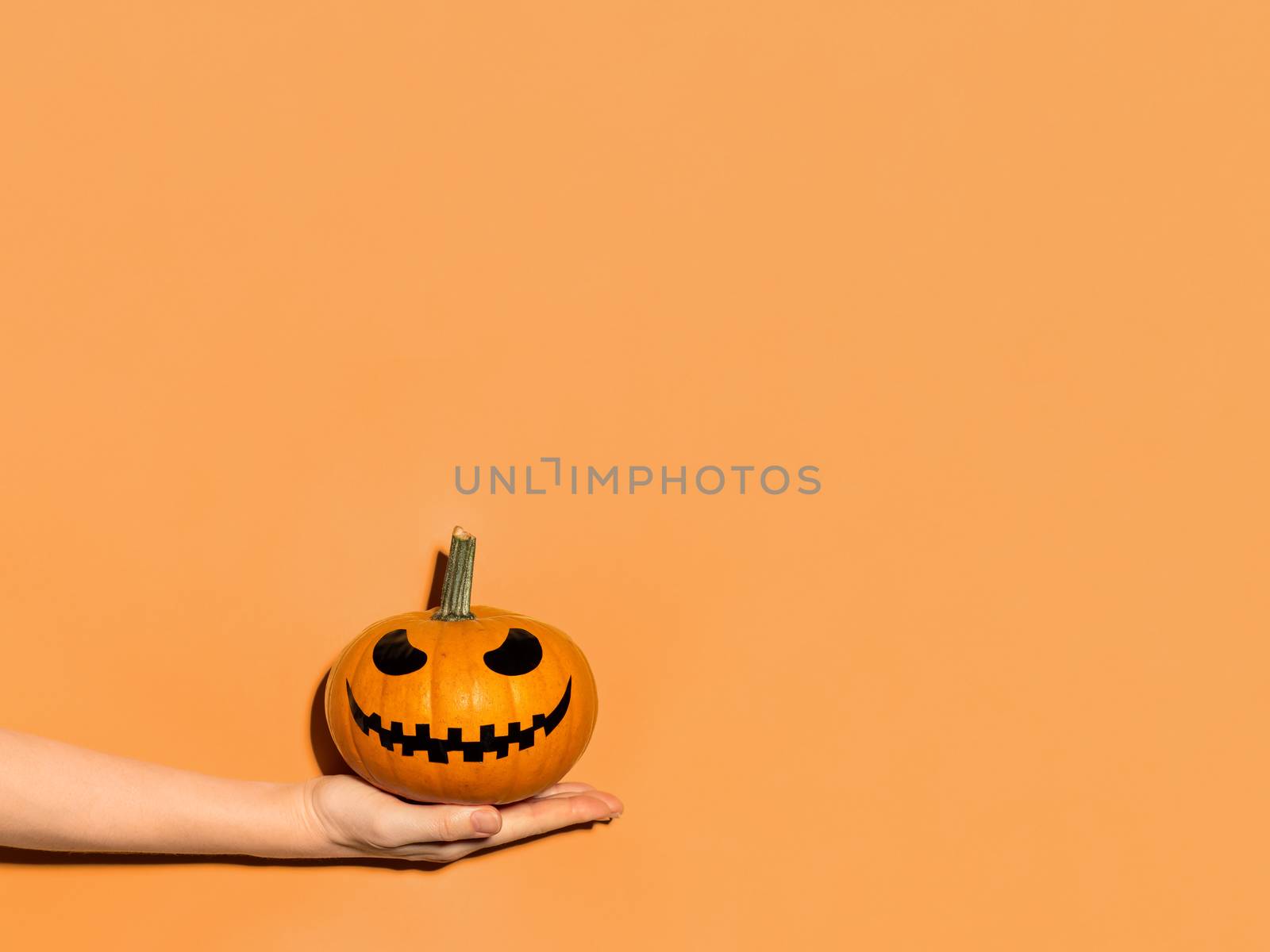 Halloween pumpkin in hand on orange background. by fascinadora