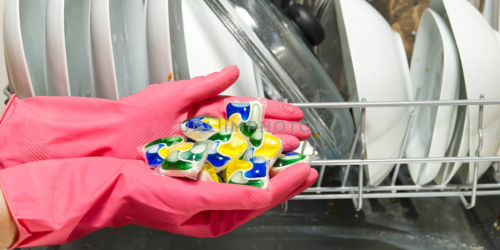 Dishwasher Detergents in hands. hands in pink golvs holds dishwasher gel capsules. Brilliant cleanliness. Capsule for the dishwasher.