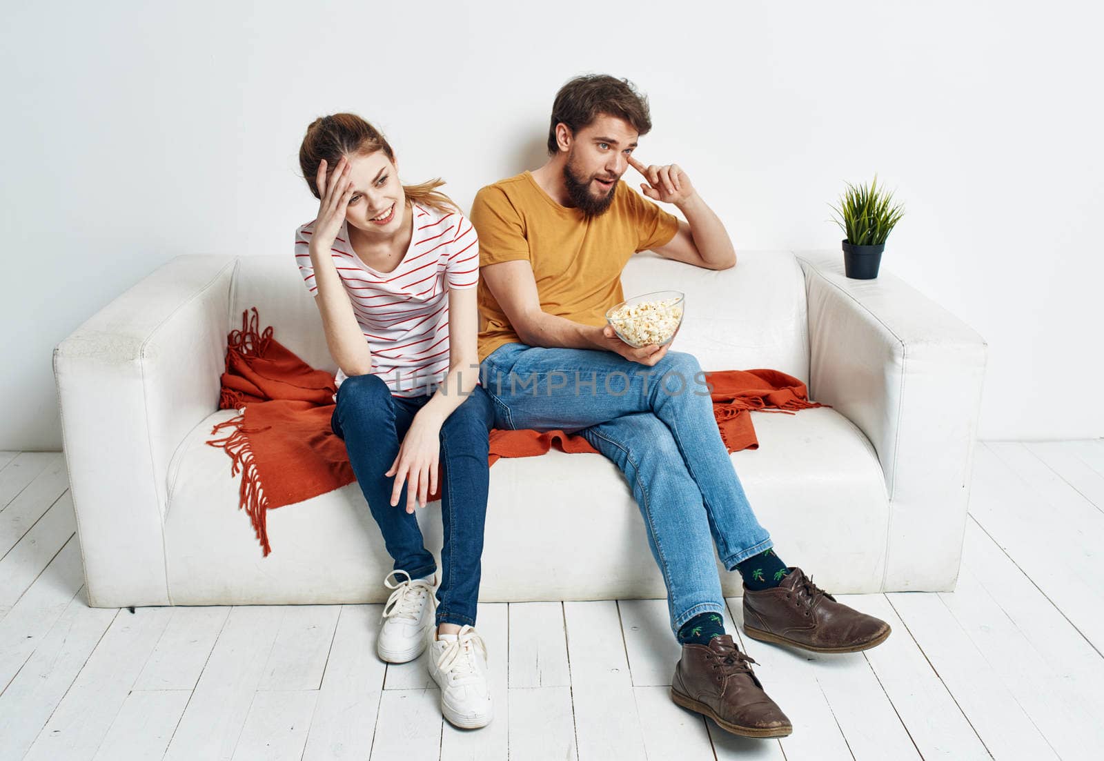 A man and a woman In a bright room sit on the couch with popcorn in a plate emotions friends green flower in a pot. High quality photo