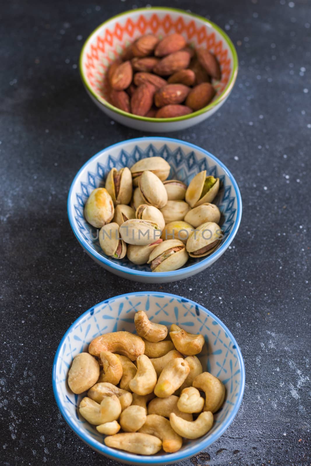 Nuts in bowls on the table, almonds, cashews and coasted nuts on the blue background. by Taidundua