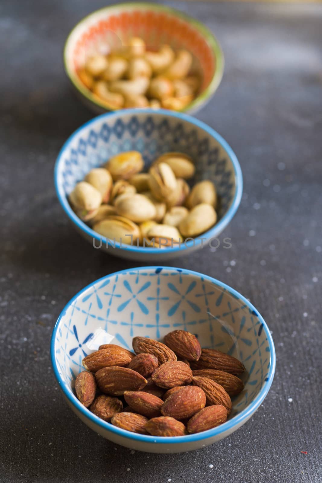 Nuts in bowls on the table, almonds, cashews and coasted nuts on the blue background. Colorful nuts set.