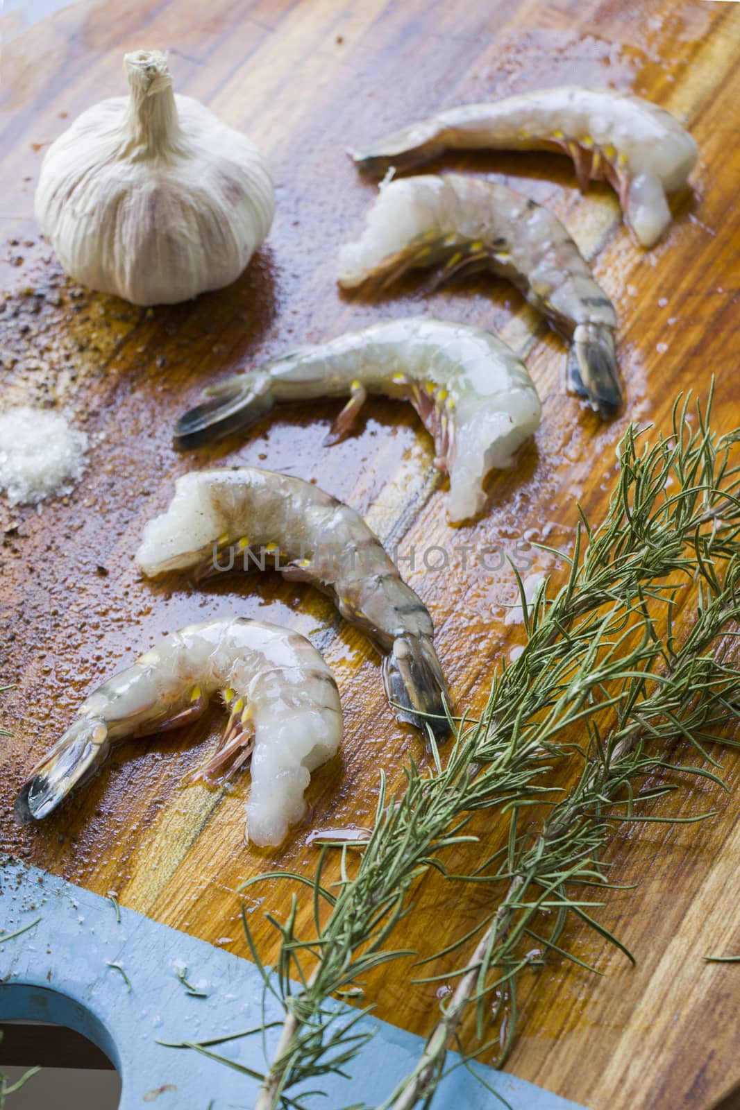 Raw shrimps on the wooden board with salt, dry pepper and rosemary by Taidundua