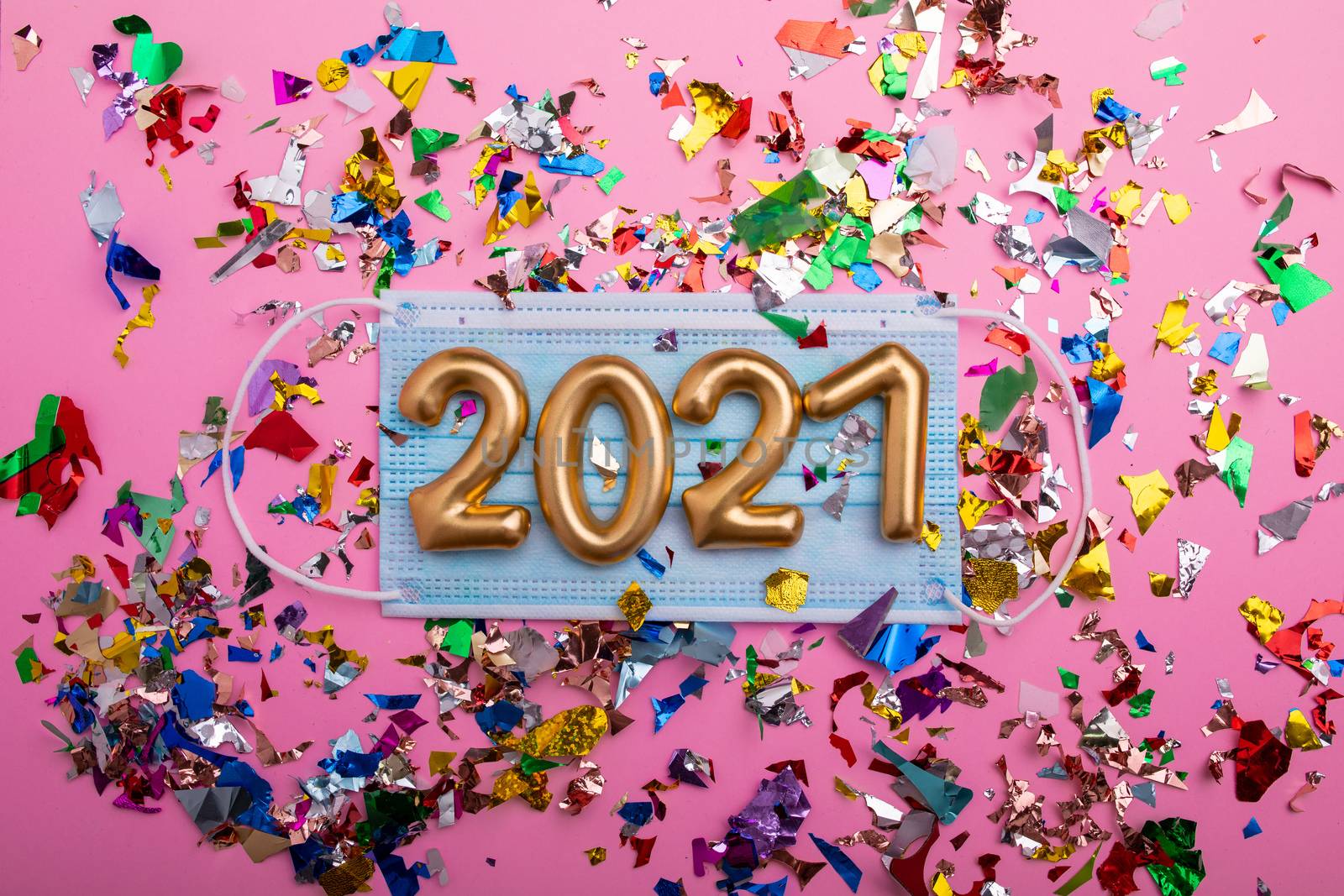 Gold numbers 2021 on face mask, pink background and confetti. Happy new pandemic year