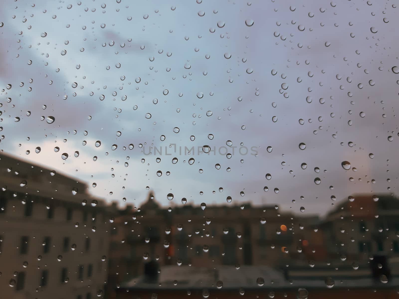 Genova, Italy - 10/22/2020: Water​ rain​ drops​ on​ glass​ background.​ Rain​ drops​ on​ a​ Windows. Hdden sunset in autumn after rain.