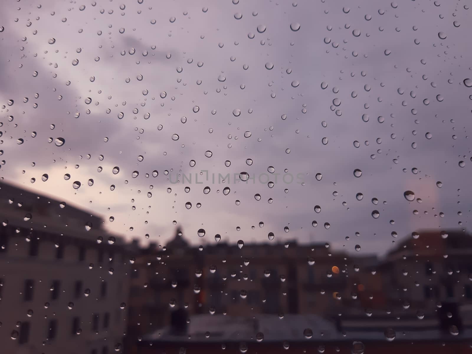 Genova, Italy - 10/22/2020: Water​ rain​ drops​ on​ glass​ background.​ Rain​ drops​ on​ a​ Windows. Hdden sunset in autumn after rain.