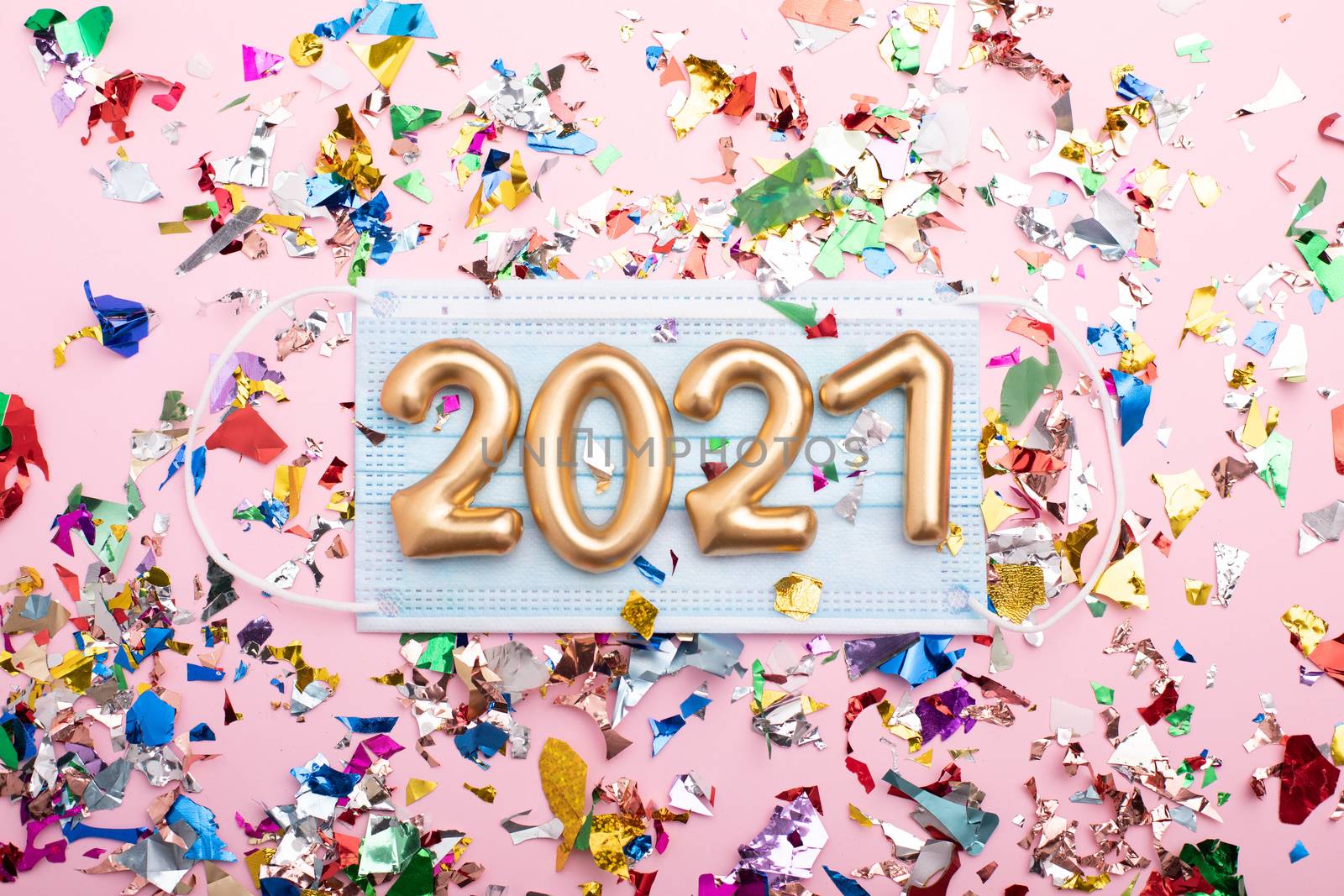 Gold numbers 2021 on face mask, pink background and confetti. Happy new pandemic year