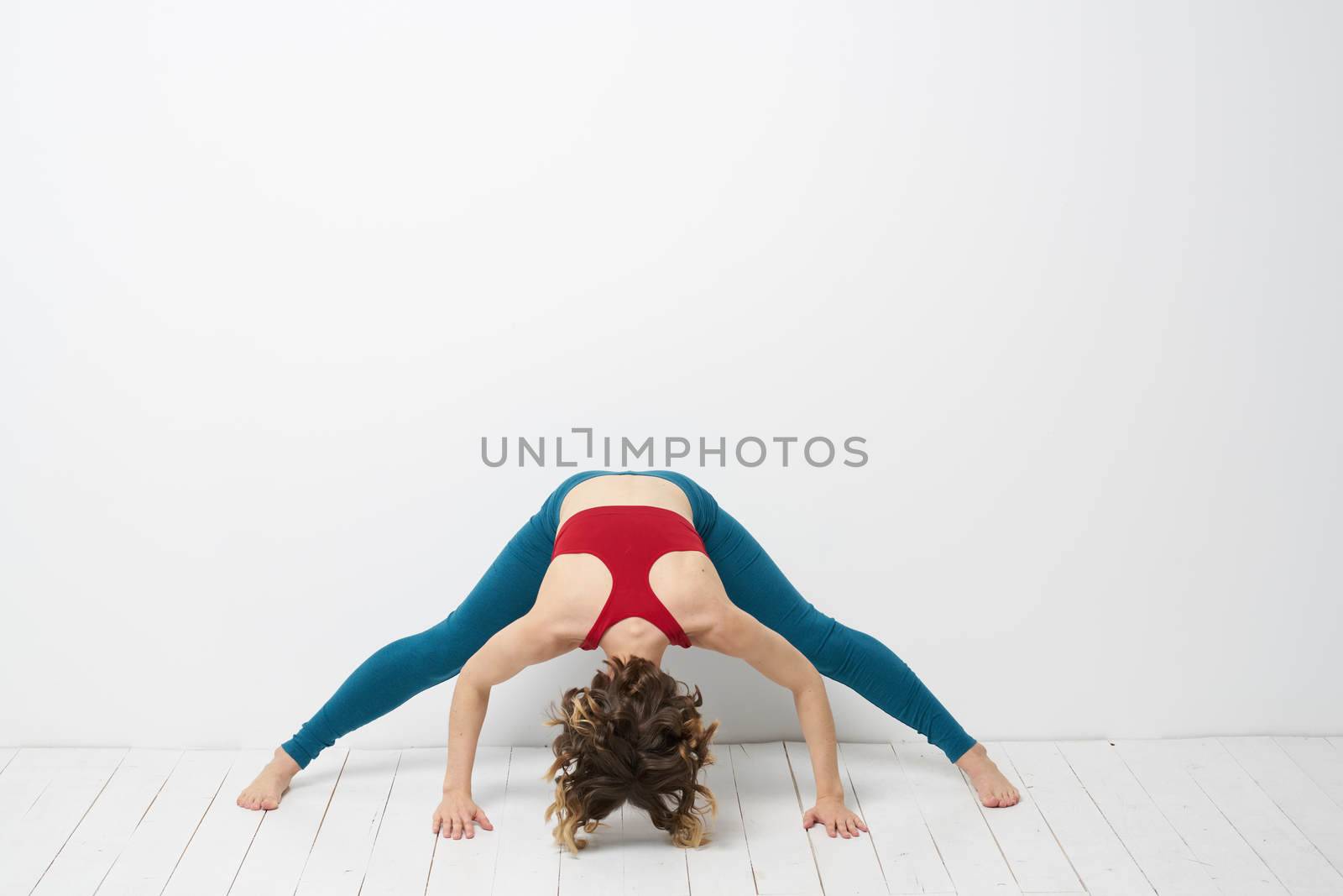 sports woman in a bright room doing yoga in full growth blue leggings and a red tank top. High quality photo