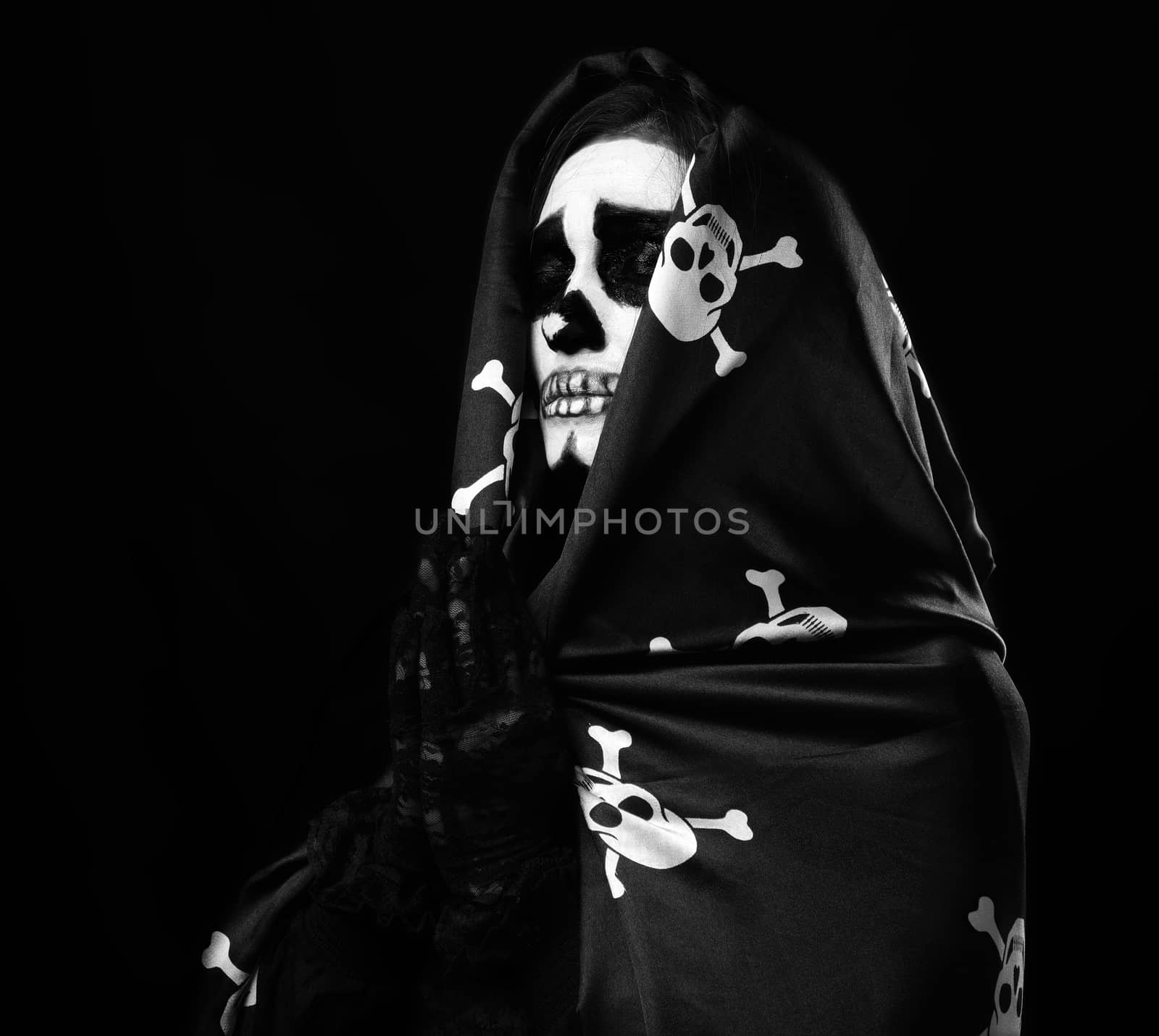 woman with skeleton make-up stands in prayer pose, wearing black silk cloak cape, black background