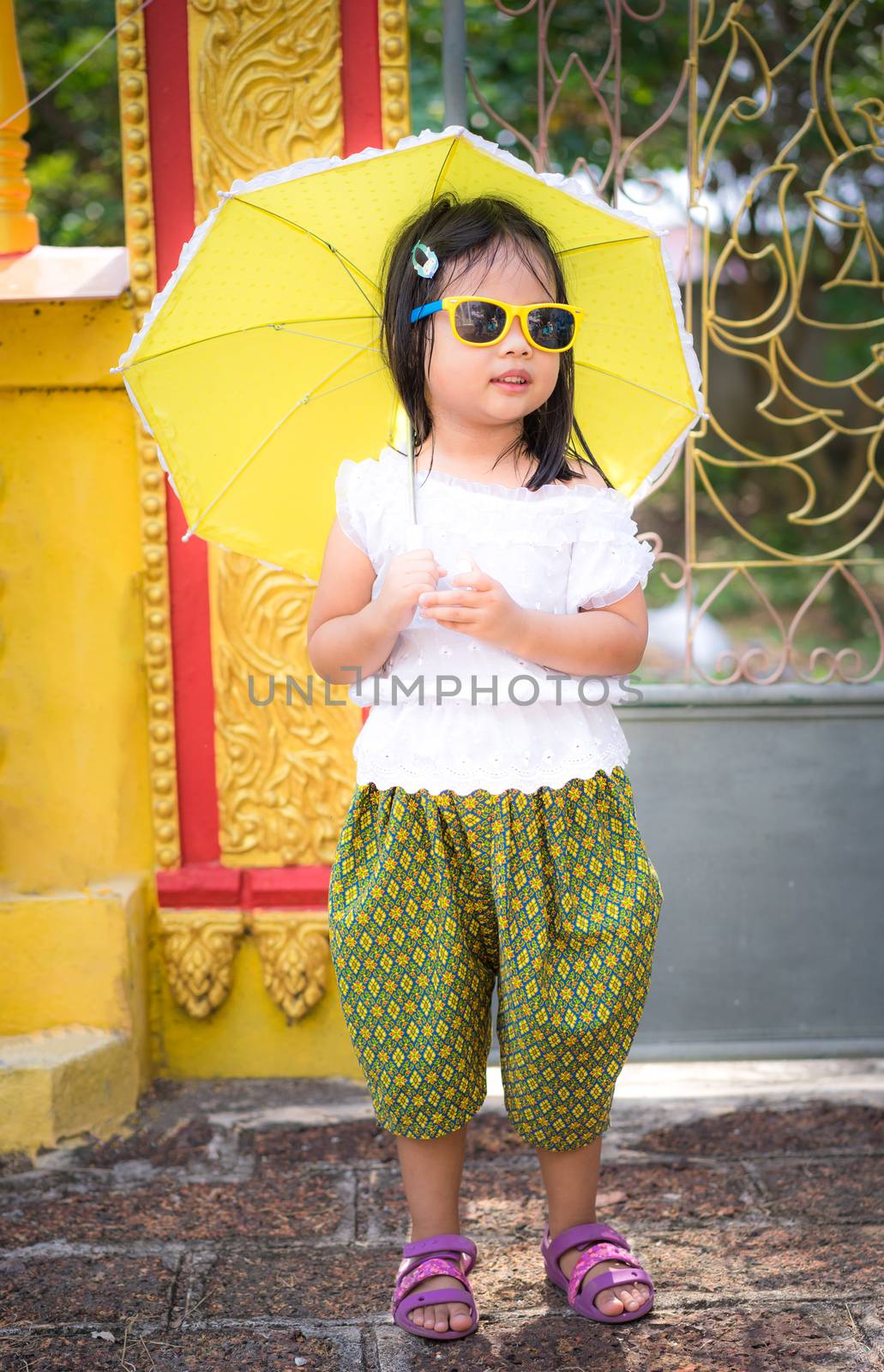 happy asian little girl in Thai period dress with sunglasses and umbrella in temple