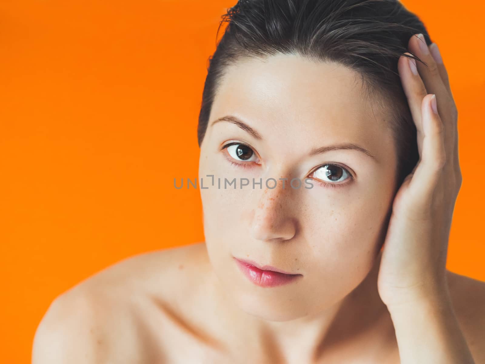 Portrait of woman with freckles on orange monochrome background. No make up. Natural beauty on bright and colorful backdrop. Banner with copy space.