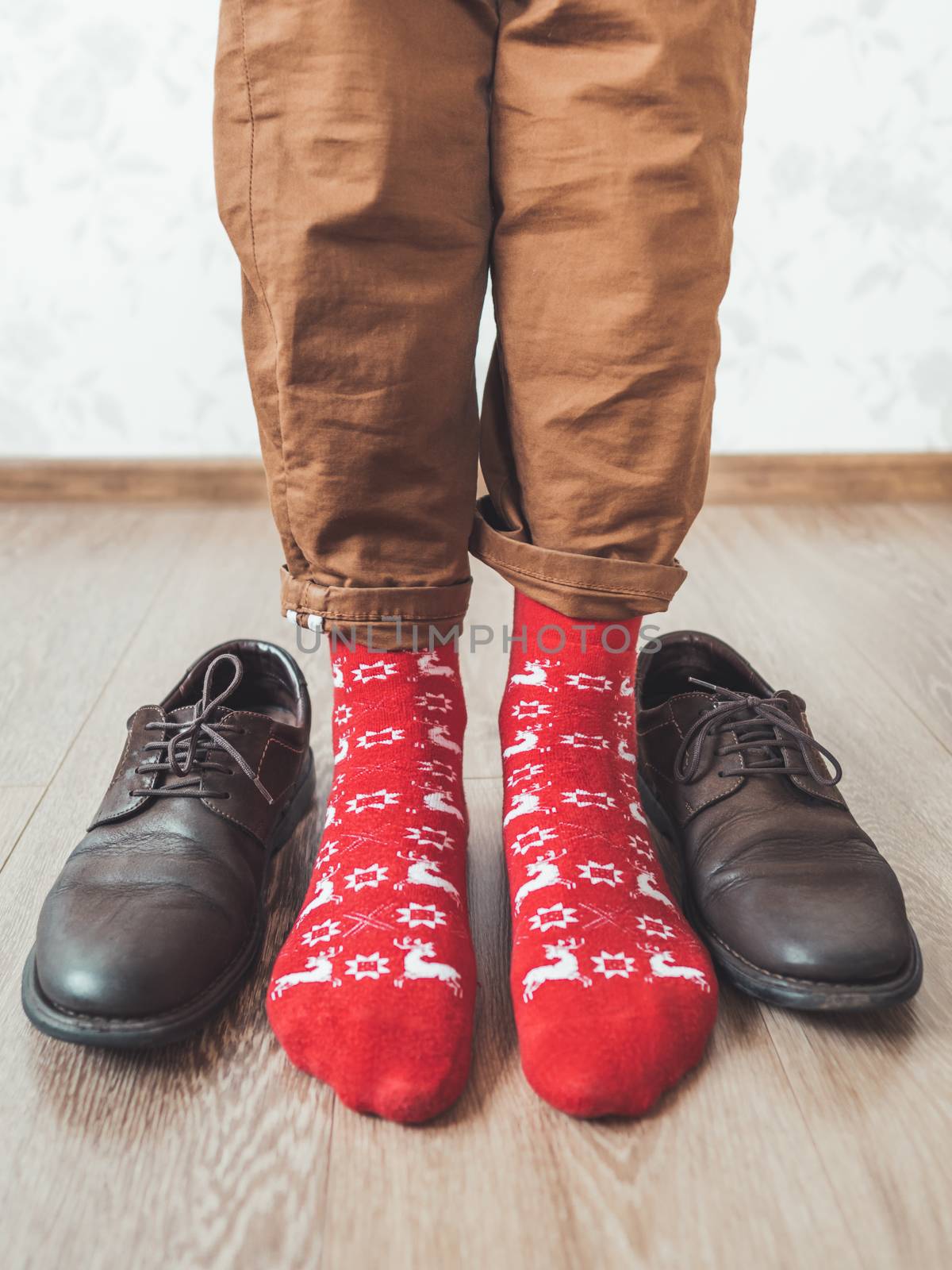 Young man in chinos trousers and bright red socks with reindeers on them is ready to wear sude shoes. Scandinavian pattern. Winter holiday spirit. Casual outfit for New Year and Christmas celebration.