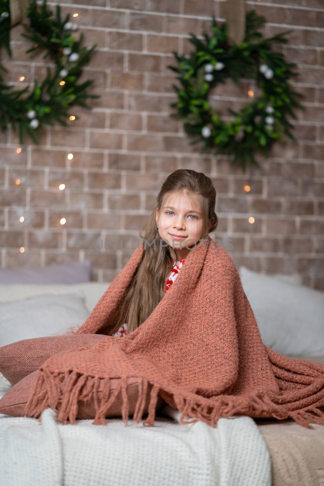 A little girl keeps warm under a cozy knitted blanket.