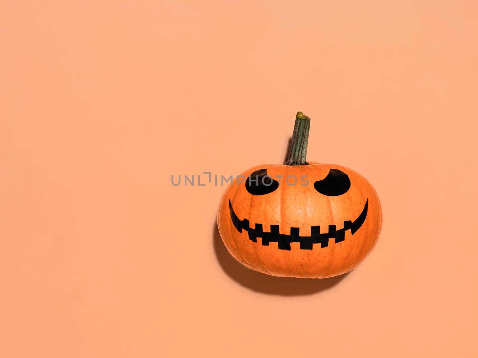 Halloween pumpkin on orange background. Halloween concept with copy space for text or design. Hard light. Jack-o-lantern laughing face on bright orange squash