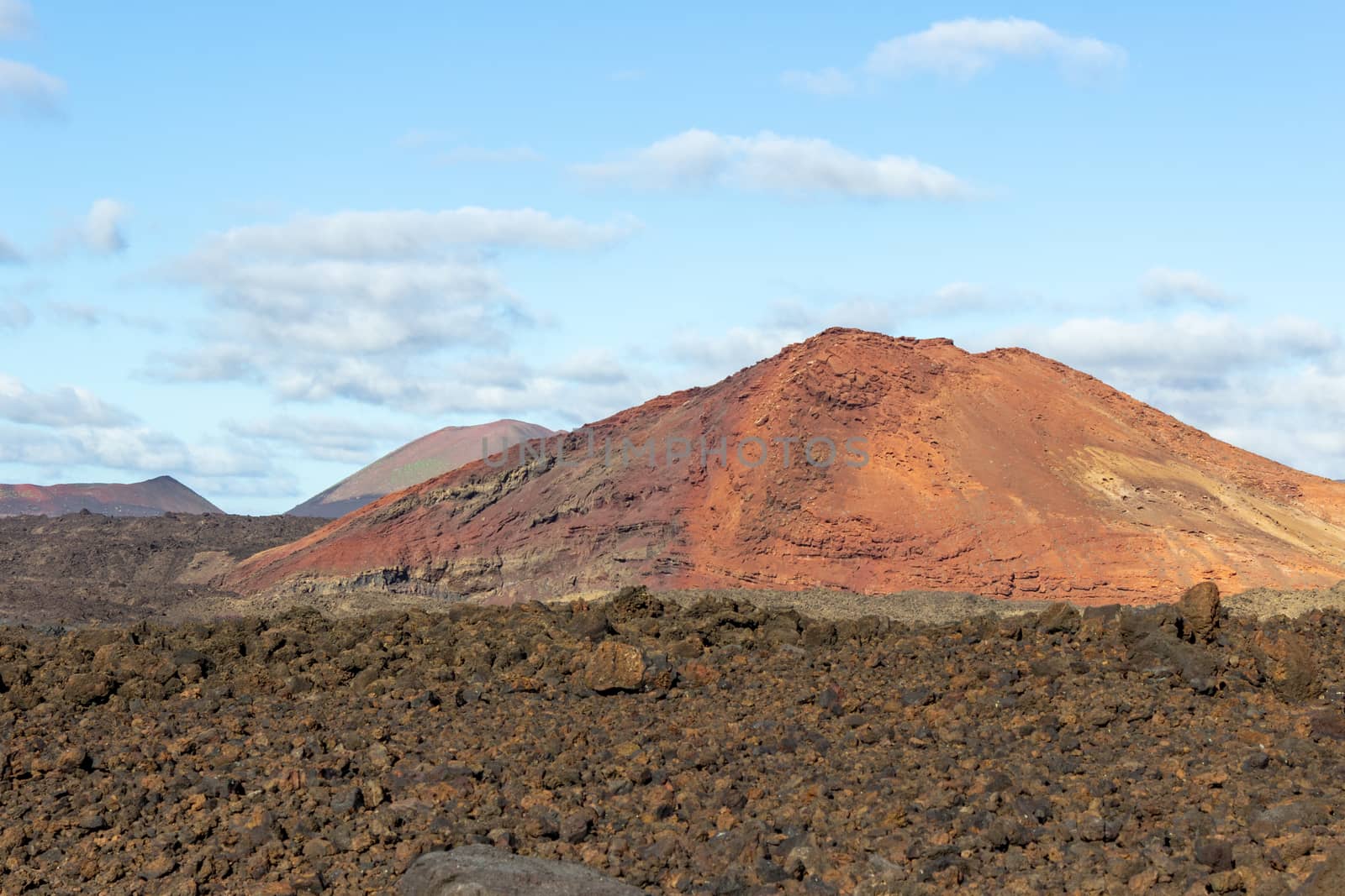 Volcanic landscape with lava field in the foreground and mountain range with different red and brown colours in the background on canary island Lanzarote, Spain