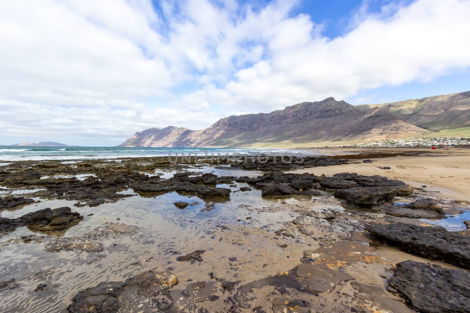 Coastline and sand beach Playa de Famara with mountain range and ocean waves in the north west of canary island Lanzarote, Spain