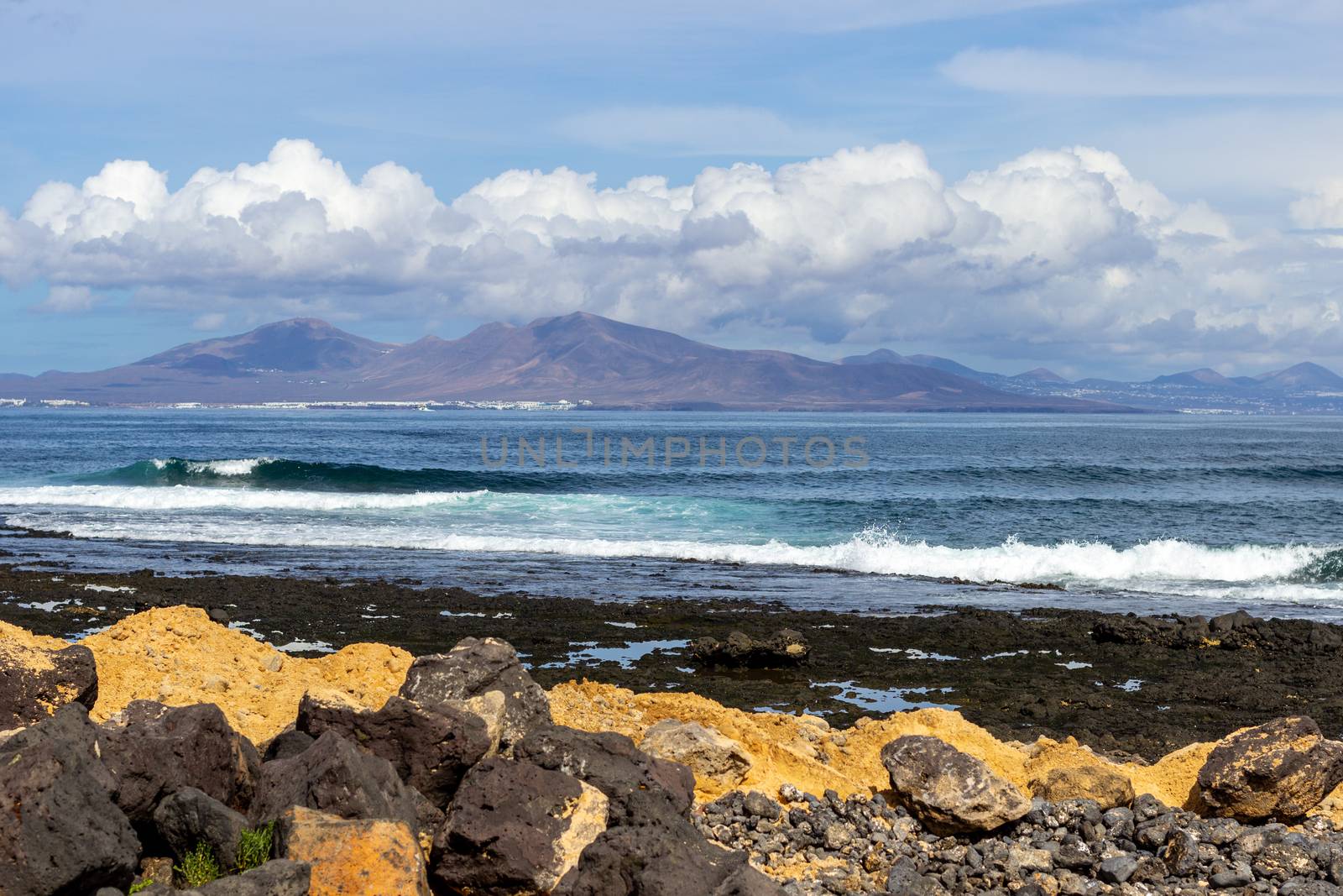 Panoramic view at the coastline of Corralejo on canary island Fuerteventura, Spain with  lava rocks and rough sea with waves and canary island Lanzarote in the  background
