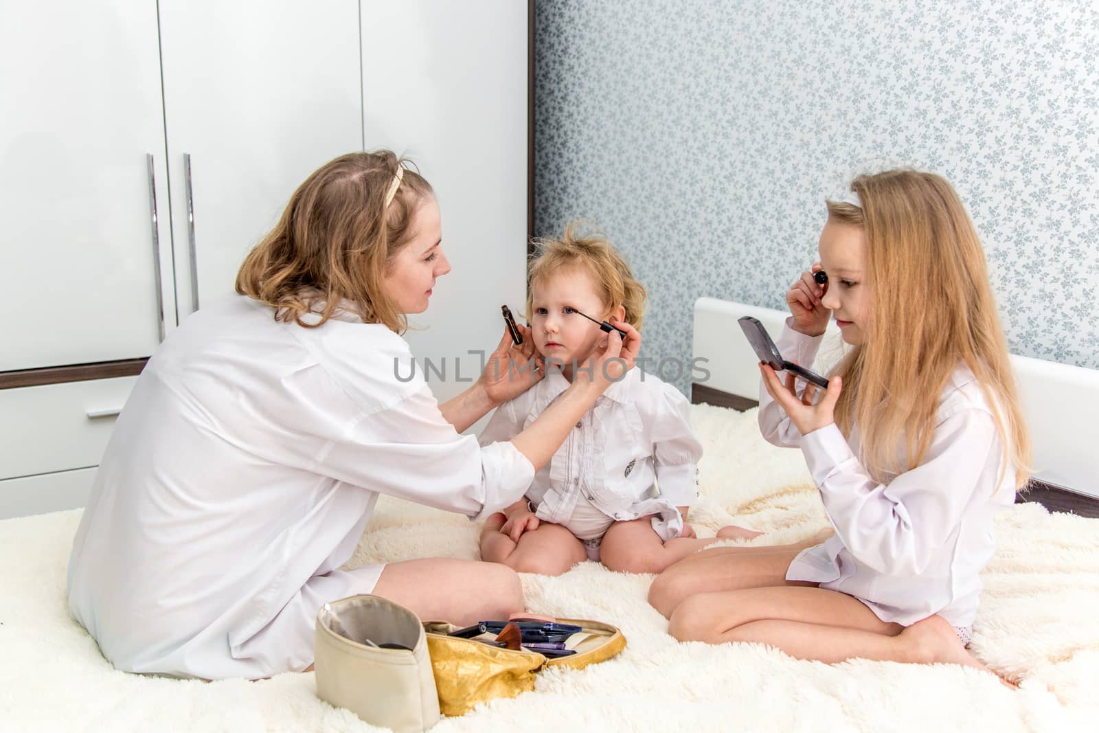 Portrait of mom and her daughters doing makeup to each other in the bedroom  by galinasharapova