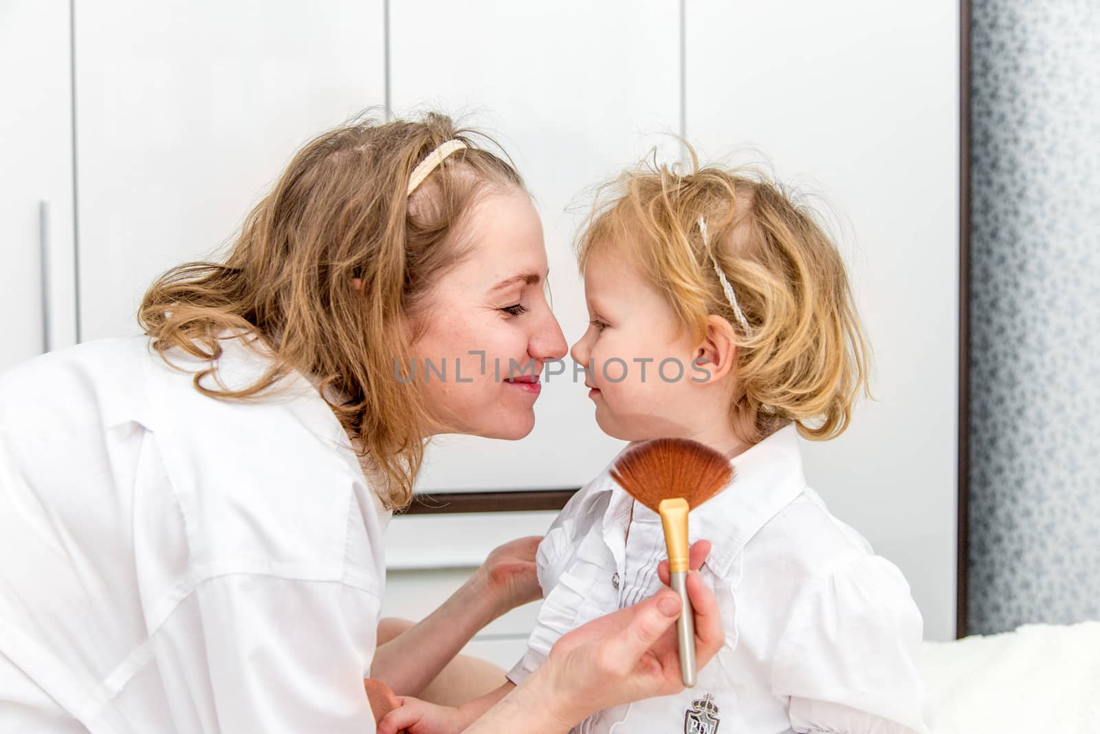 Portrait of woman doing makeup to her daughter in the bedroom on the bed.
