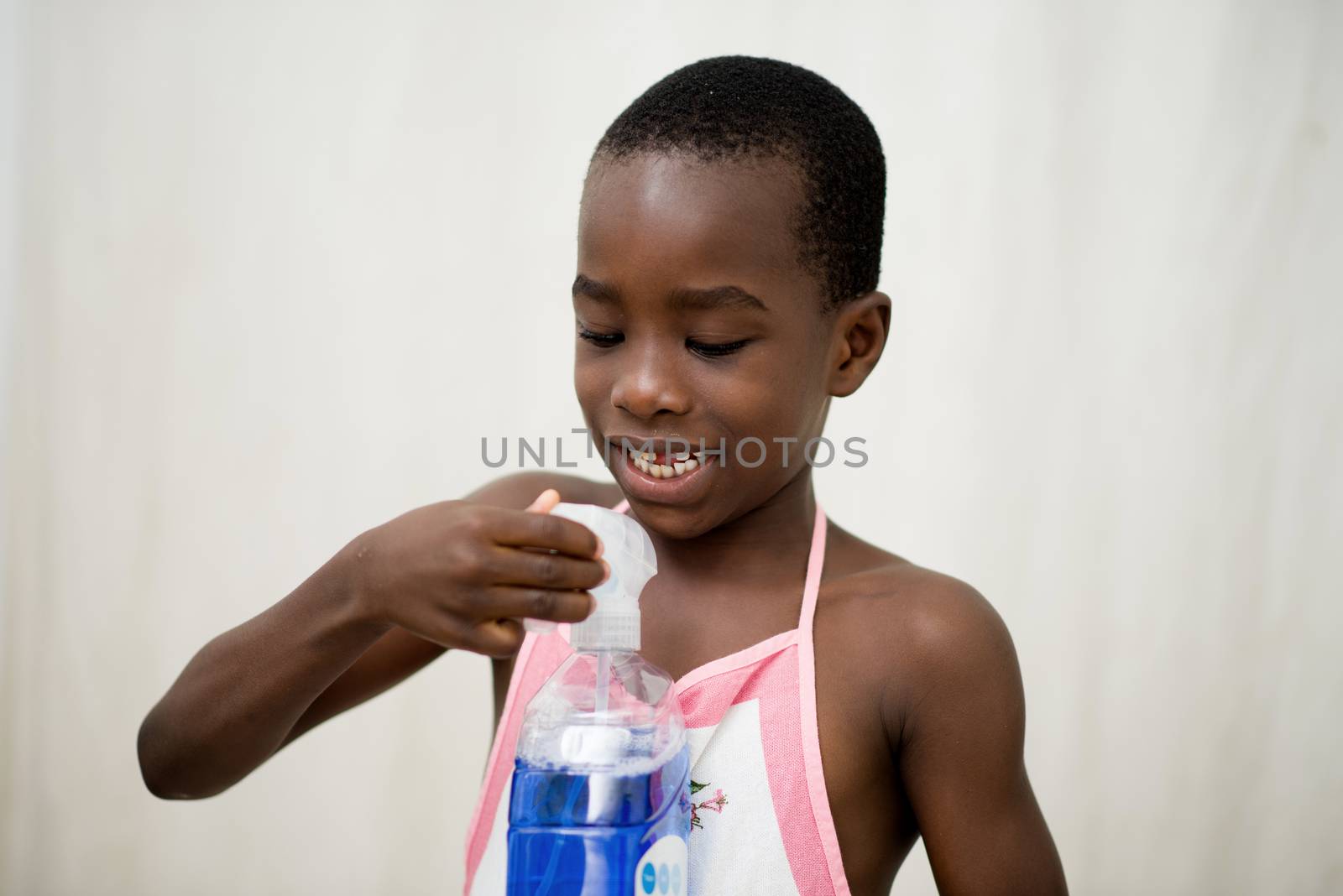 smiling little boy standing in studio and wearing apron plays with bottle of liquid soap