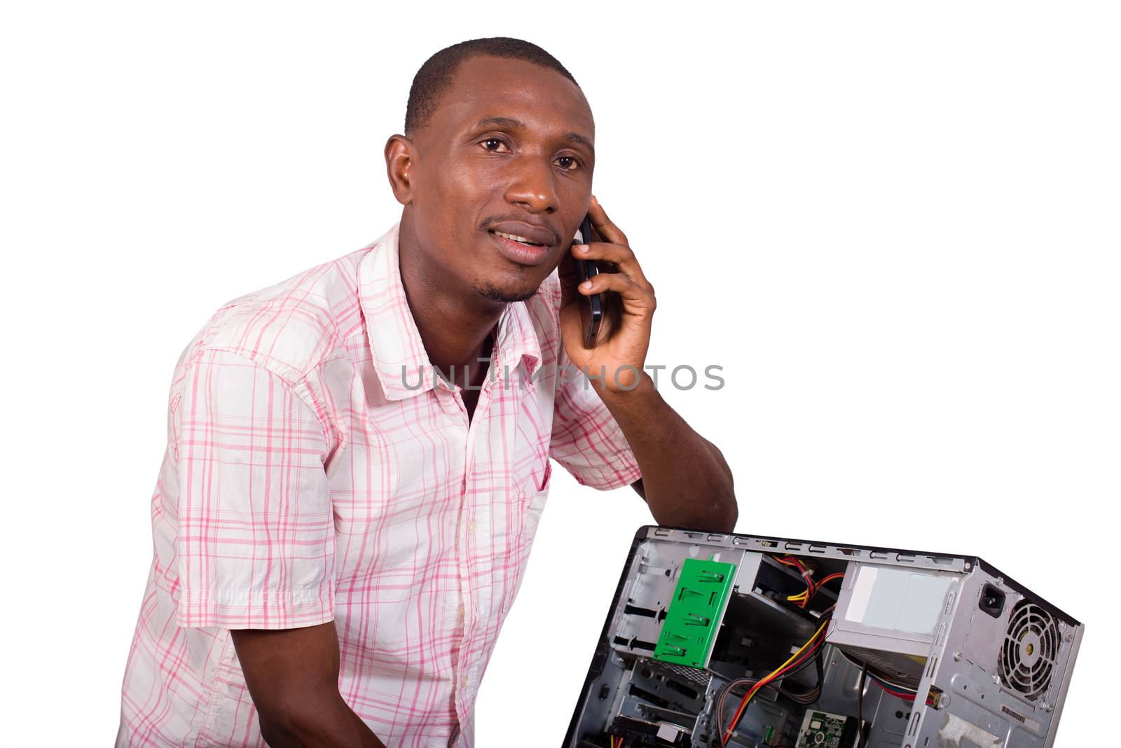 Young technician leaning against a broken computer and speaking on the phone