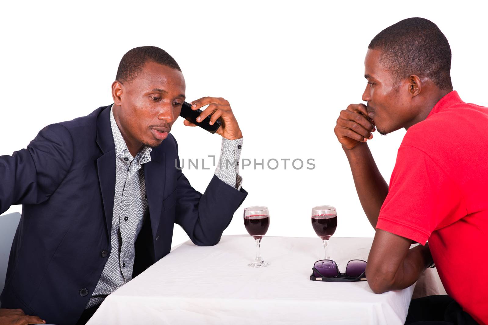 businessman sitting at restaurant with his colleague talking on the phone and drinking wine