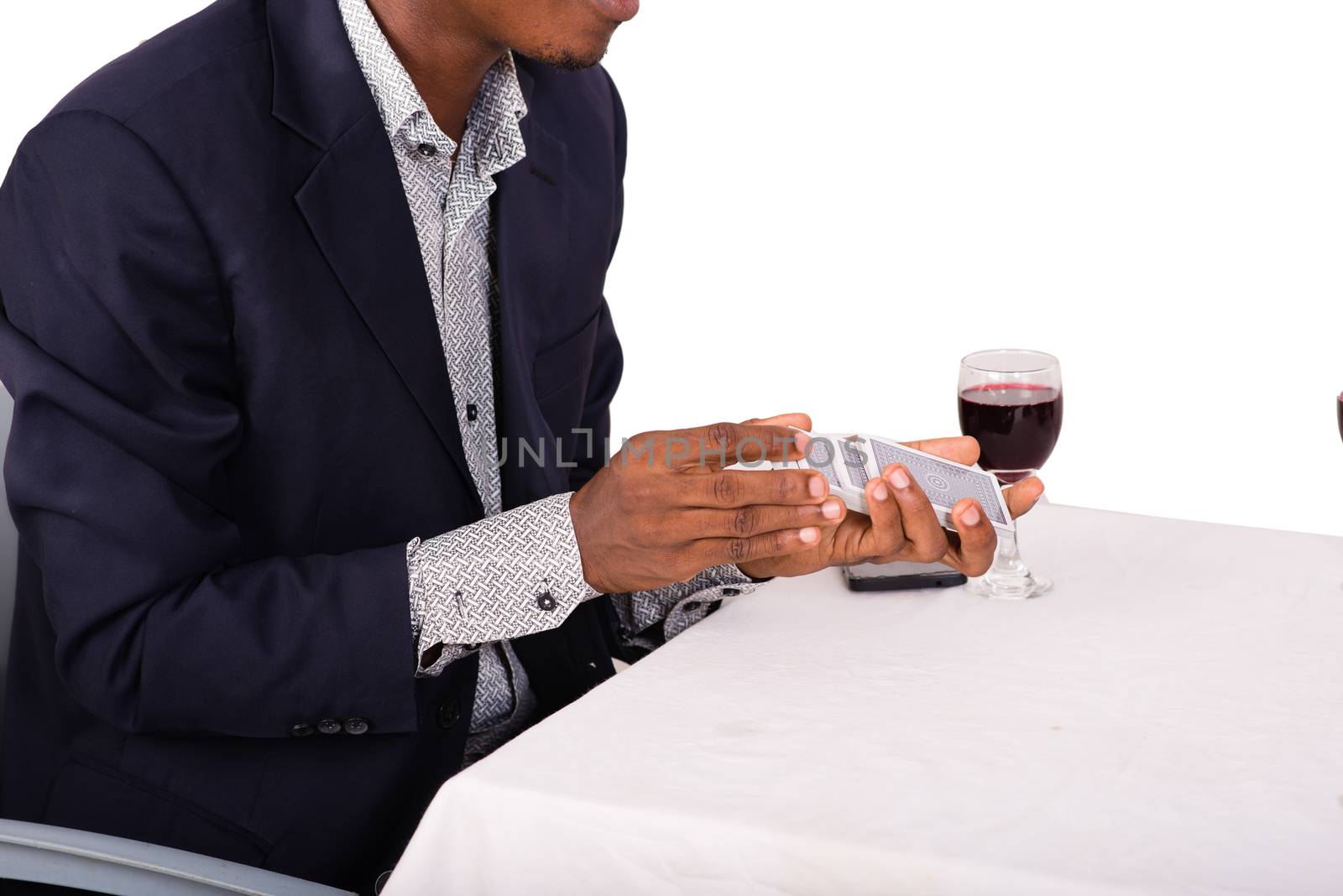 young man sitting at restaurant and pulling card game. The player holding the cards while sitting at the table with a glass of red wine.