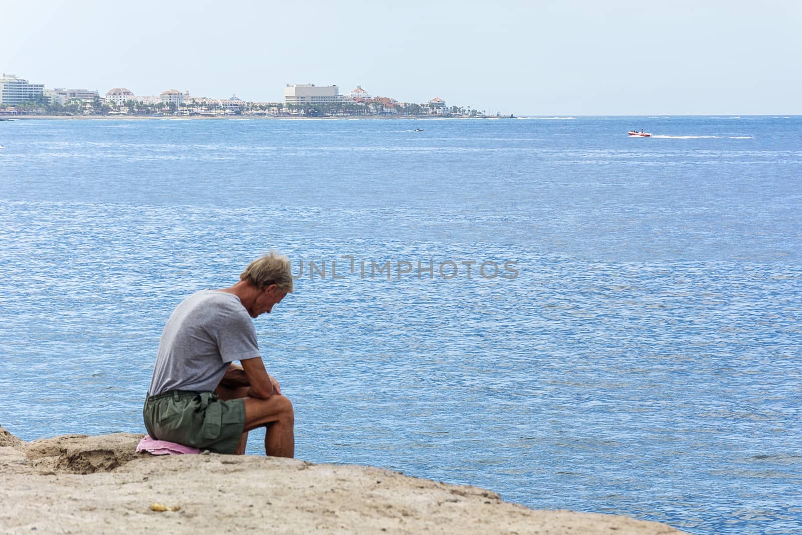 Sad old man sitting on the rocks by the sea (Spain, Tenerife) by Grommik