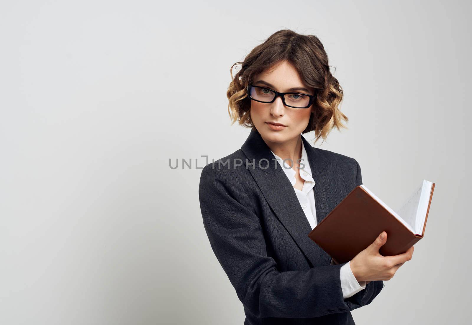 A woman in a classic suit with a book in her hands on a light background and glasses on her face business finance. High quality photo