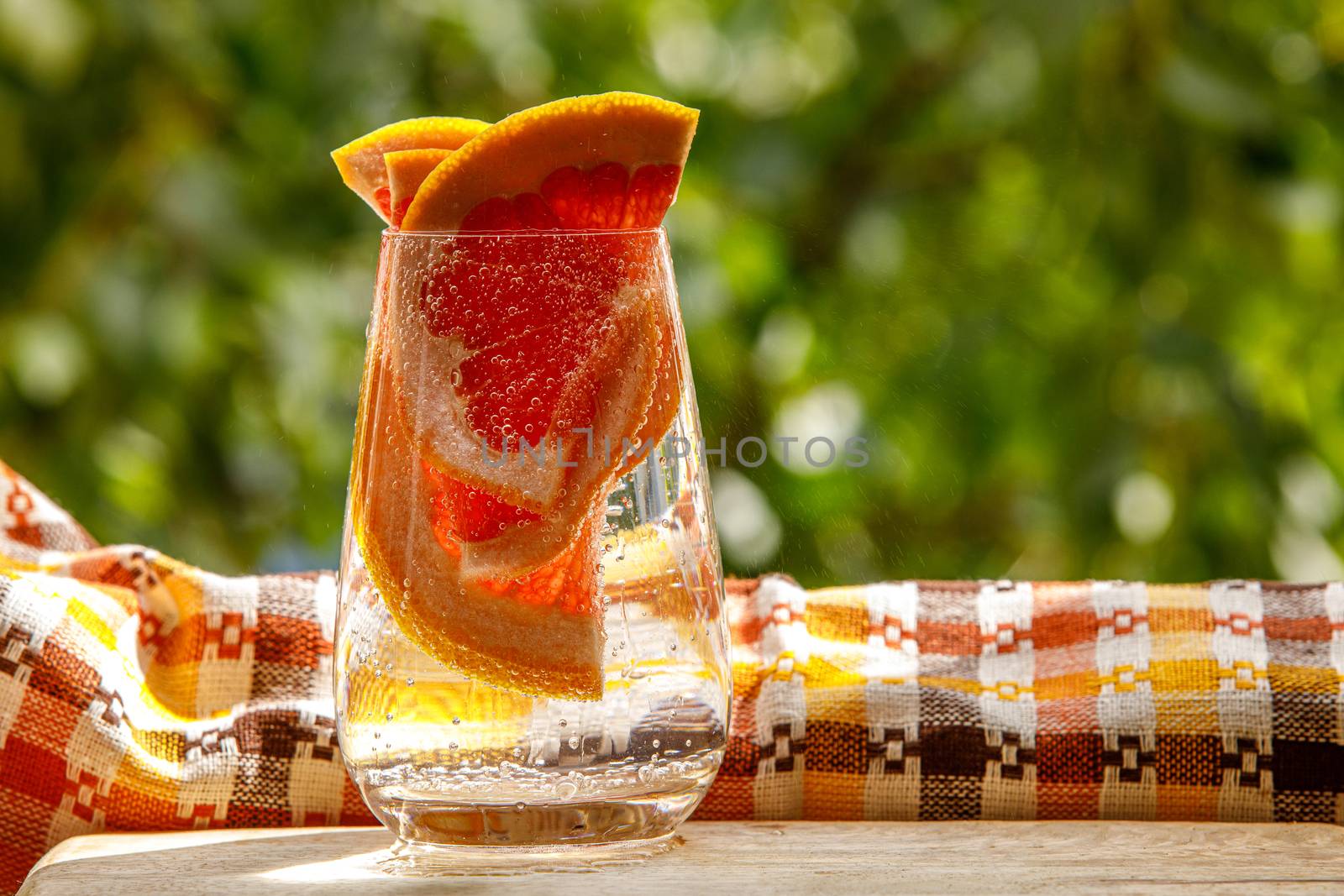 A glass of water with grapefruit in the garden background. by 9parusnikov