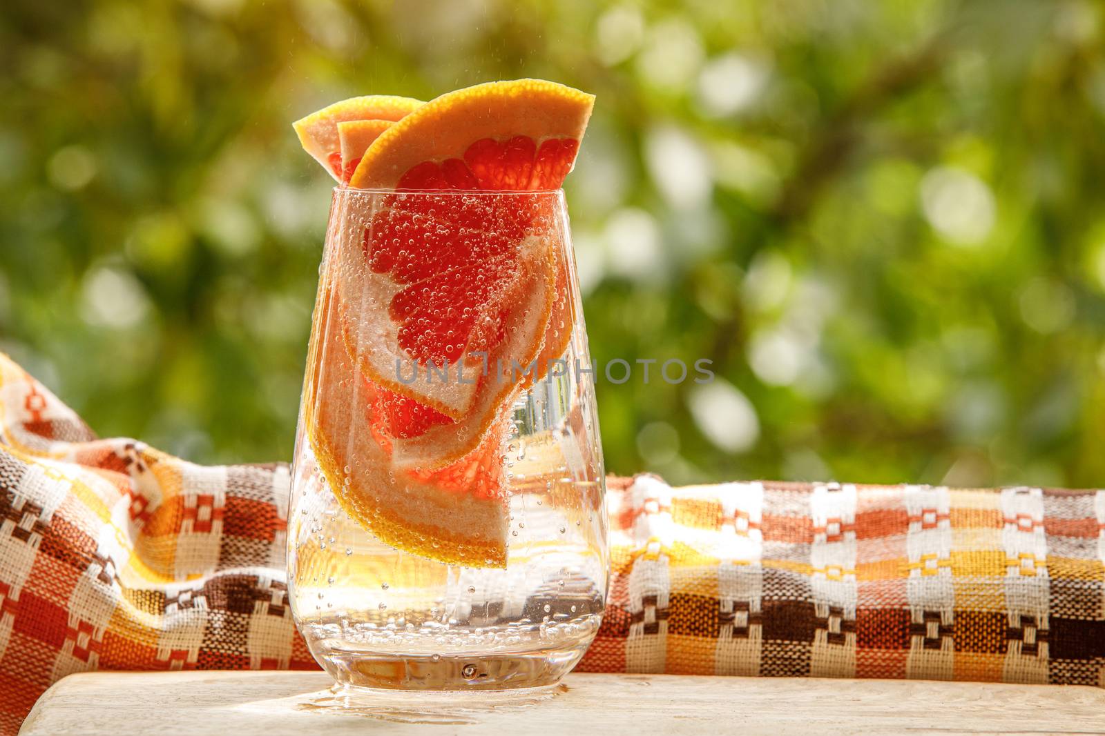 A glass of water with grapefruit in the garden background. by 9parusnikov