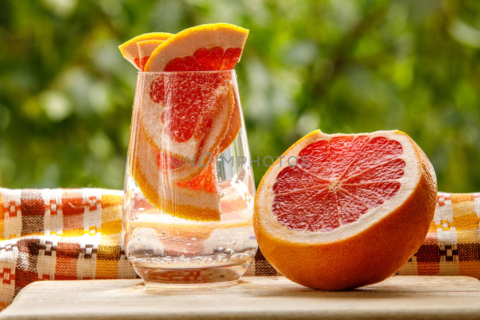 A glass of water with grapefruit in the garden background. by 9parusnikov