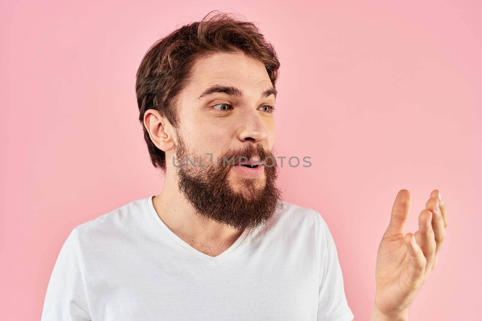Bearded man in white t-shirt gesturing with hands facial expression close up pink background. High quality photo
