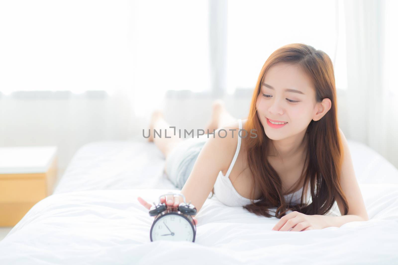 Beautiful asian young woman turn off alarm clock in morning, wake up for sleep with alarm clock, relax and lifestyle concept.