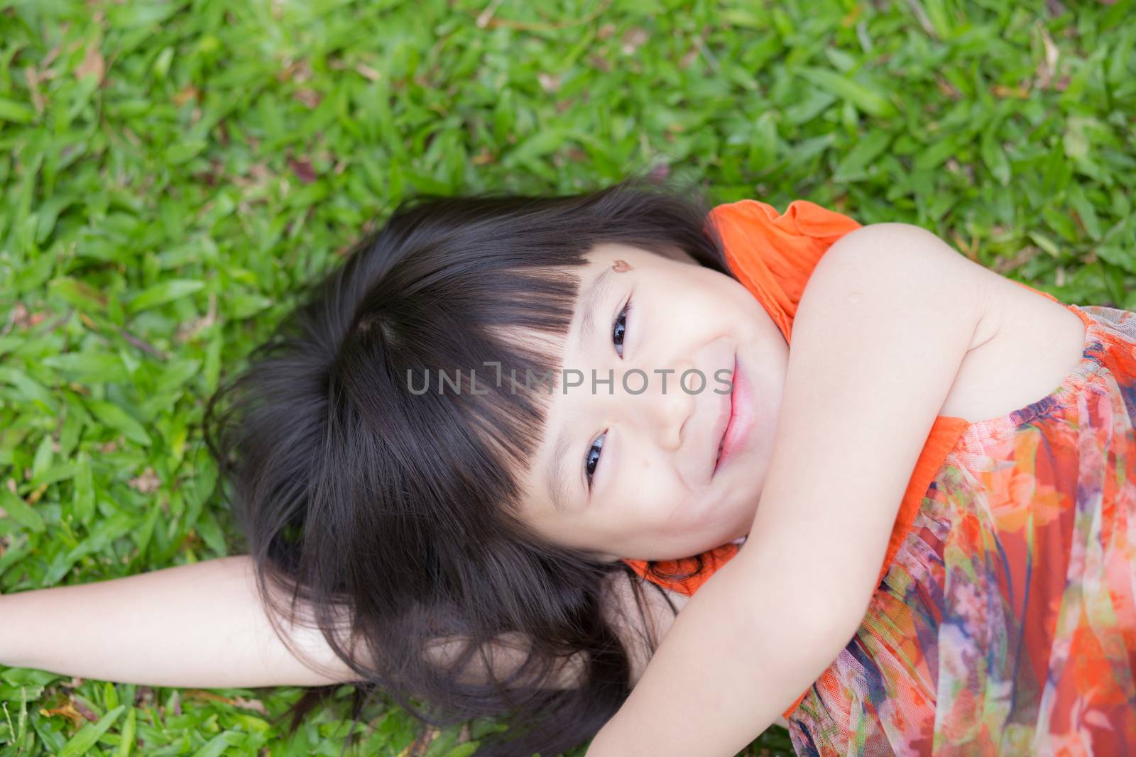 Beautiful portrait little girl asian of a smiling lying on green grass at the park, kid leisure and joyful in outdoor.