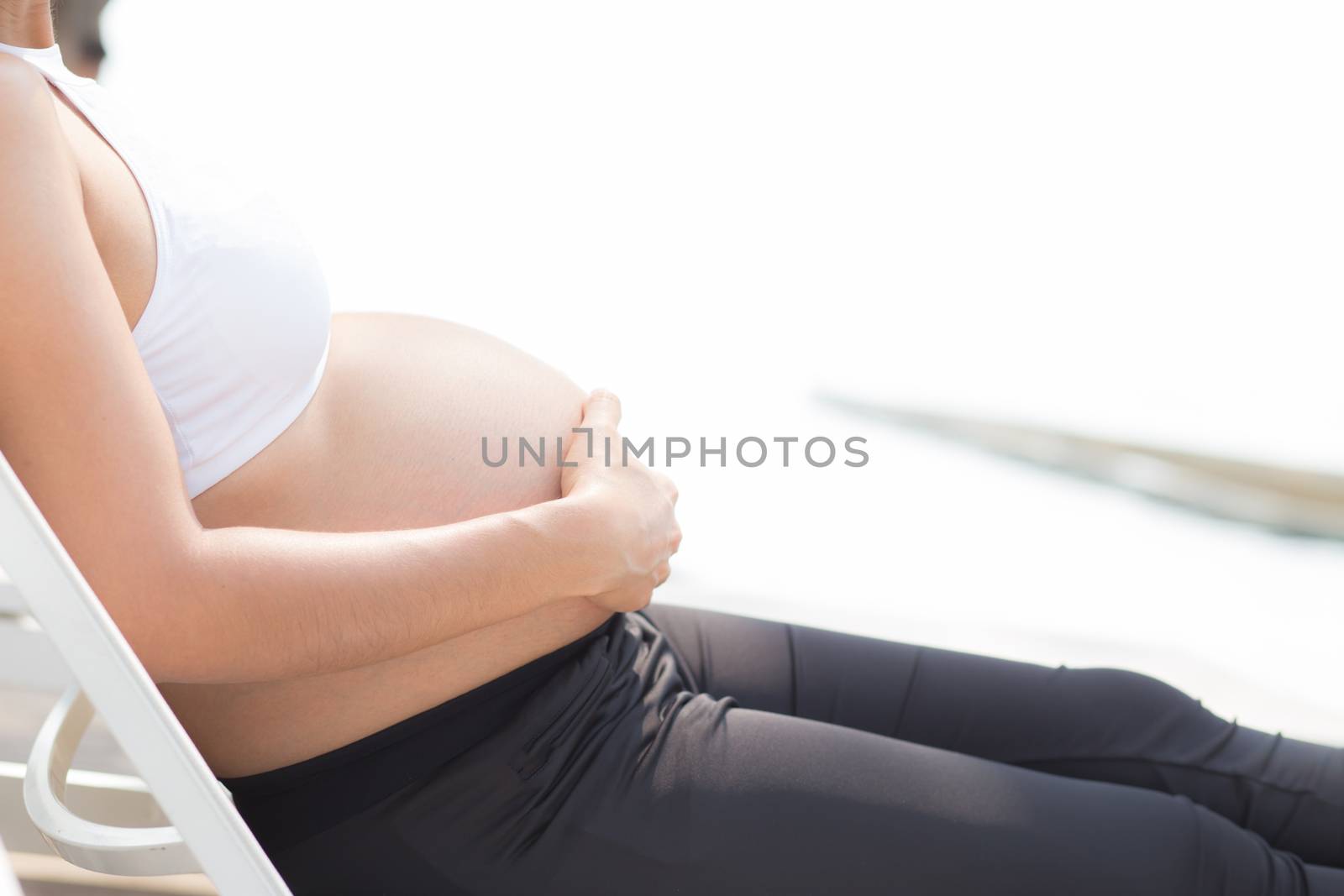 closeup beautiful pregnant asian young woman relax in the park, girl with belly sitting at swimming pool for wellness, copy space.