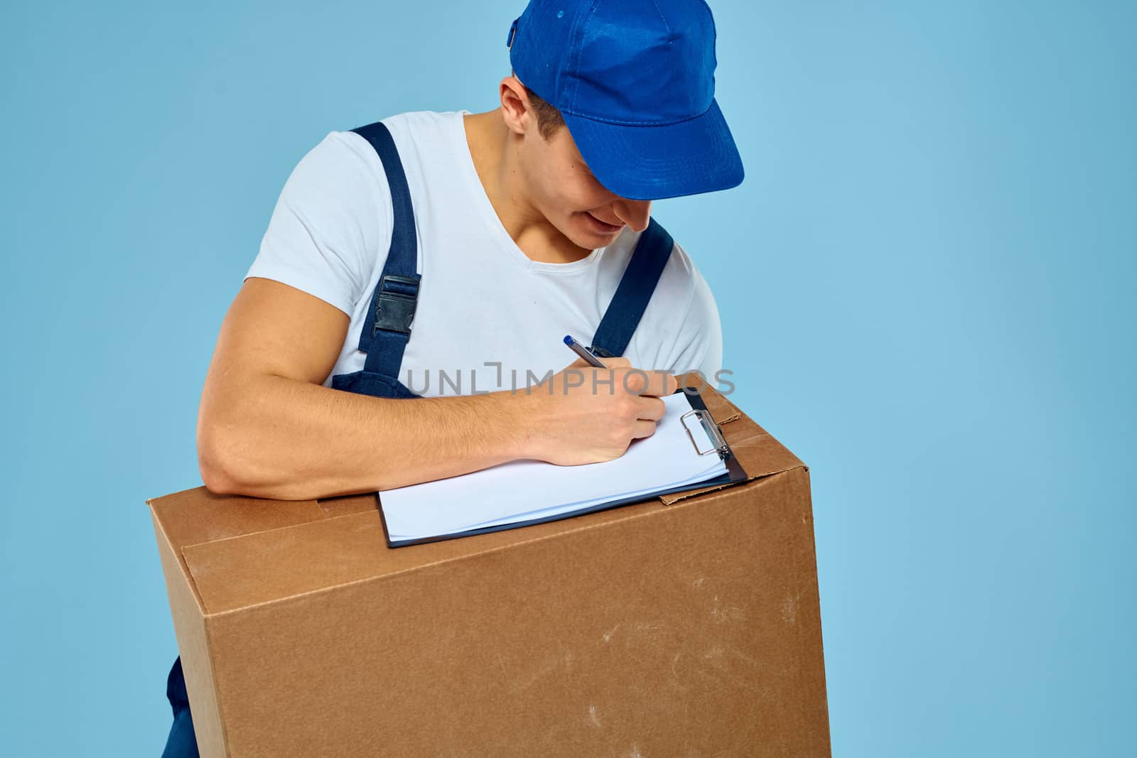 Man worker with cardboard box delivery loader lifestyle blue background by SHOTPRIME