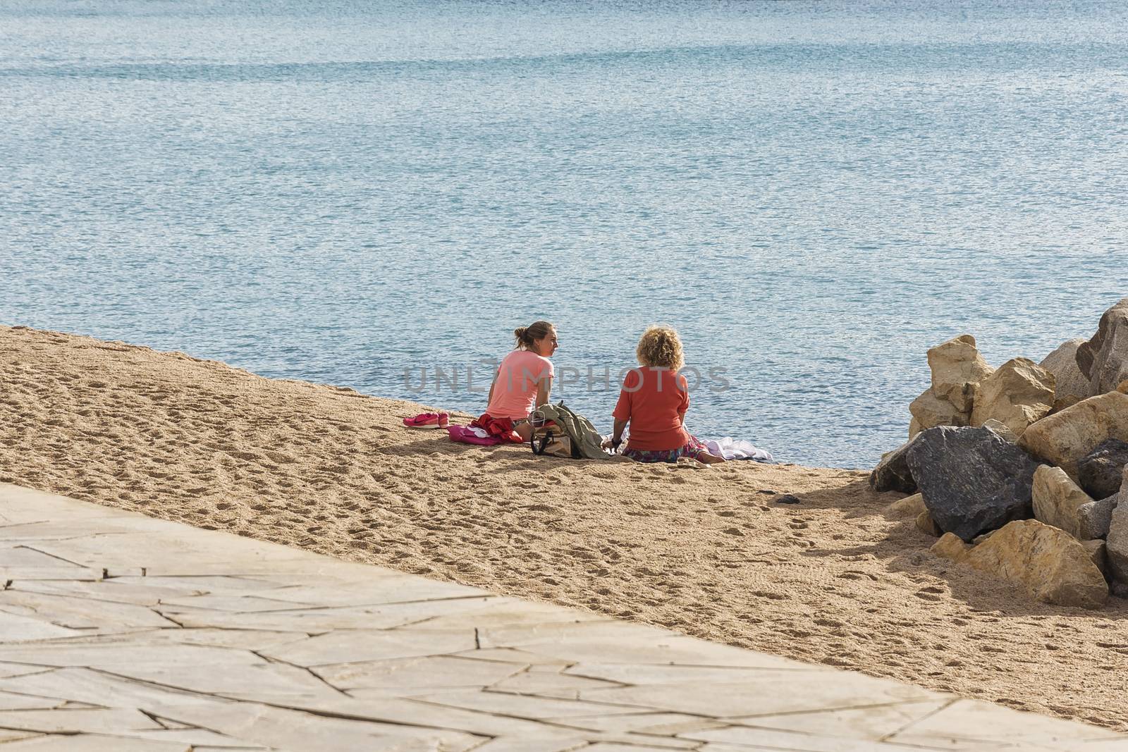 Two girls are sitting on the beach near the water and talking (B by Grommik