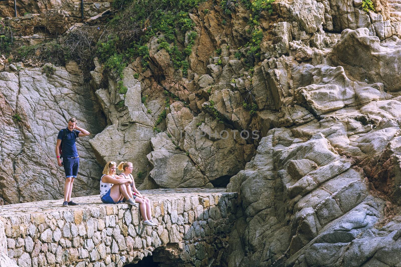 Spain, Lloret de Mar - September 22, 2017: Two girls and a guy on a stone bridge near the mountain, the girls are sitting, the guy is standing.