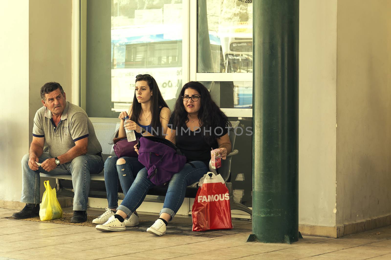 Greece, Zakynthos Island - June 17, 2016: Two young girls and an elderly man sit on a bench in a bus lazy