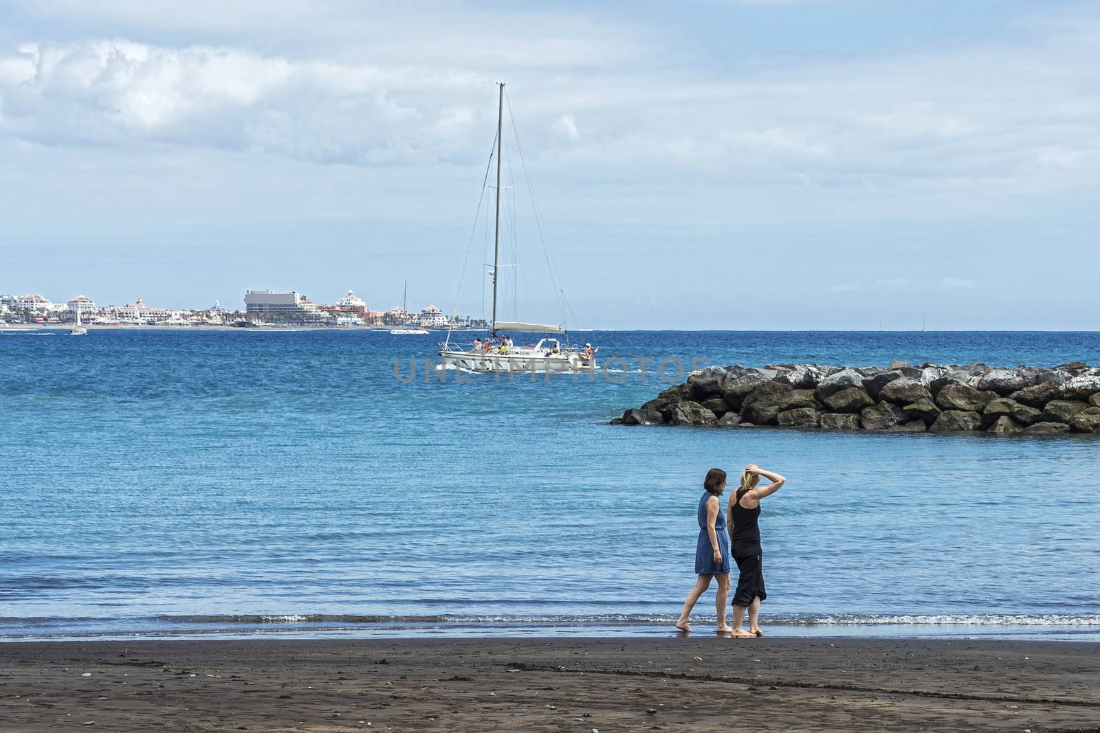 Two young women stroll along the beach near the water by Grommik