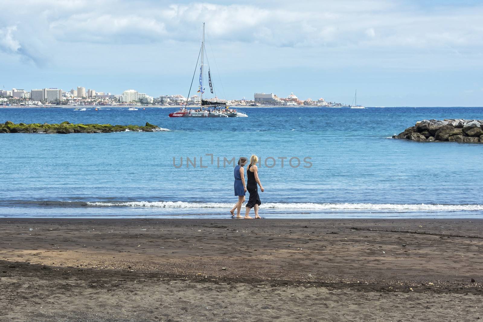 Two young women are walking on the beach near the water by Grommik