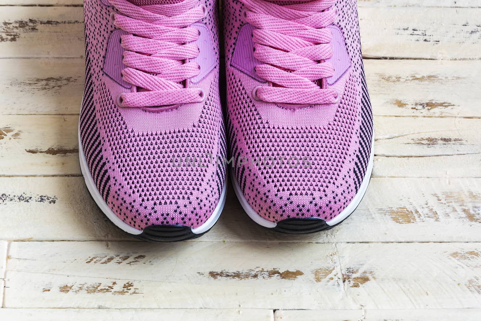 A pair of pink sneakers with pink laces stands on a wooden surfa by Grommik