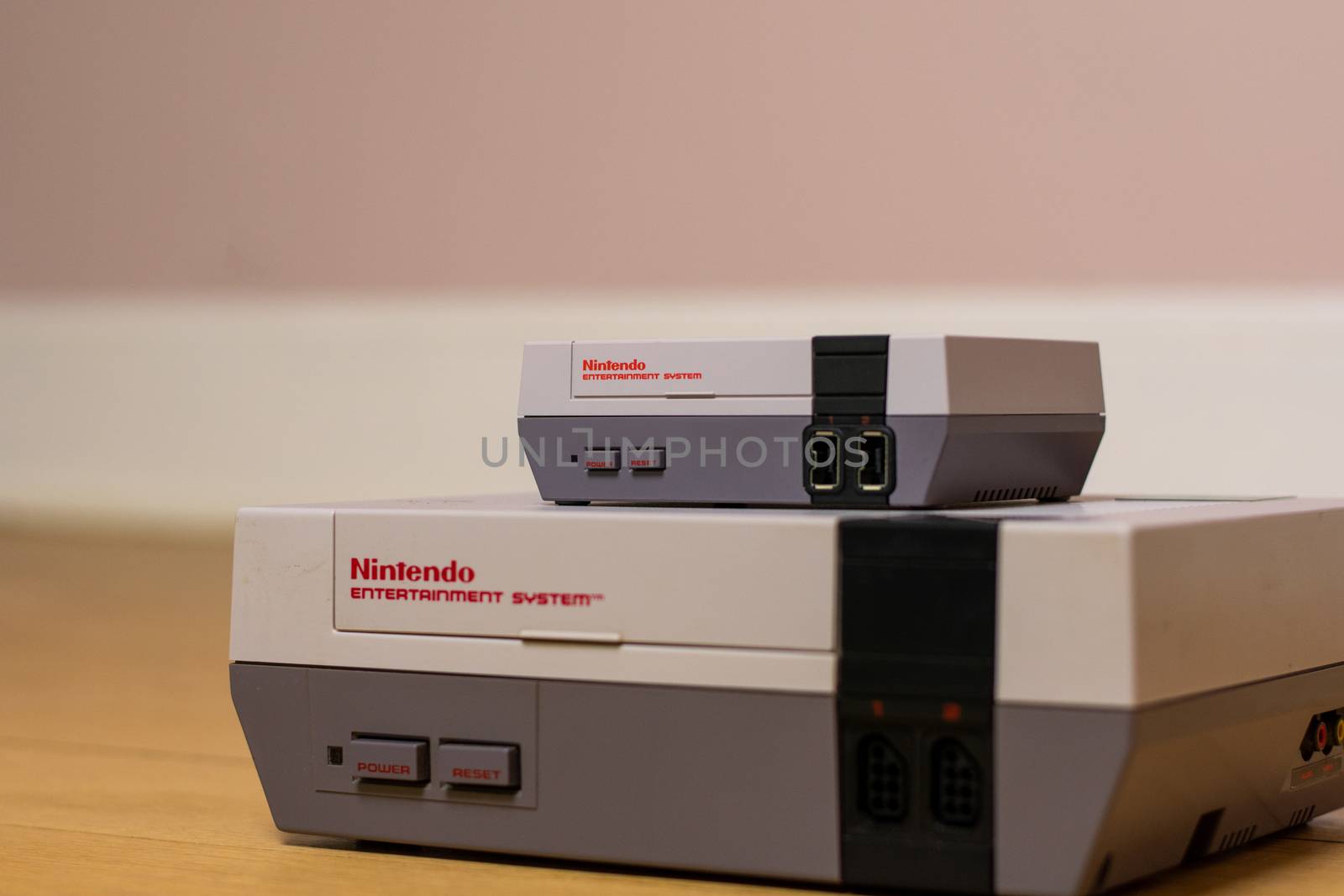 A Nintendo Entertainment System Classic Edition on Top of an Original Nintendo Entertainment System, on a wood floor. Comparison of the original NES against the NES Classic Edition