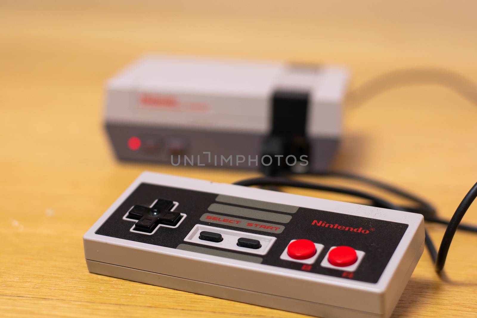 The Controller of a Nintendo Entertainment System Classic Edition Plugged Into the Console on a wooden floor, plugged into the console.