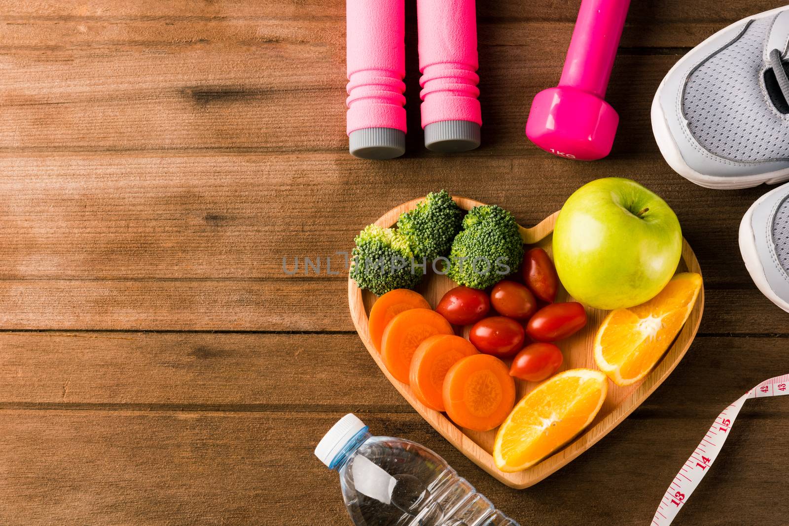 Top view of fresh fruits and vegetables in heart plate wood (apple, carrot, tomato, orange, broccoli) and dumbbells, sport shoes sports equipment on wooden table, Healthy lifestyle diet food concept
