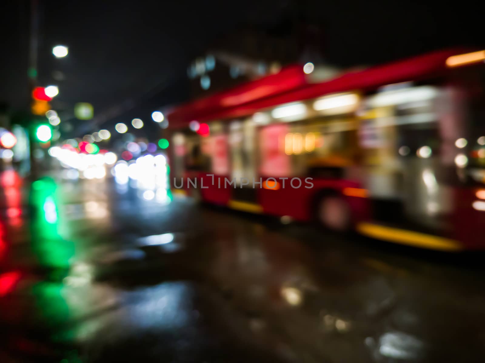 defocused night rain city street view with red bus crossing road with car traffic