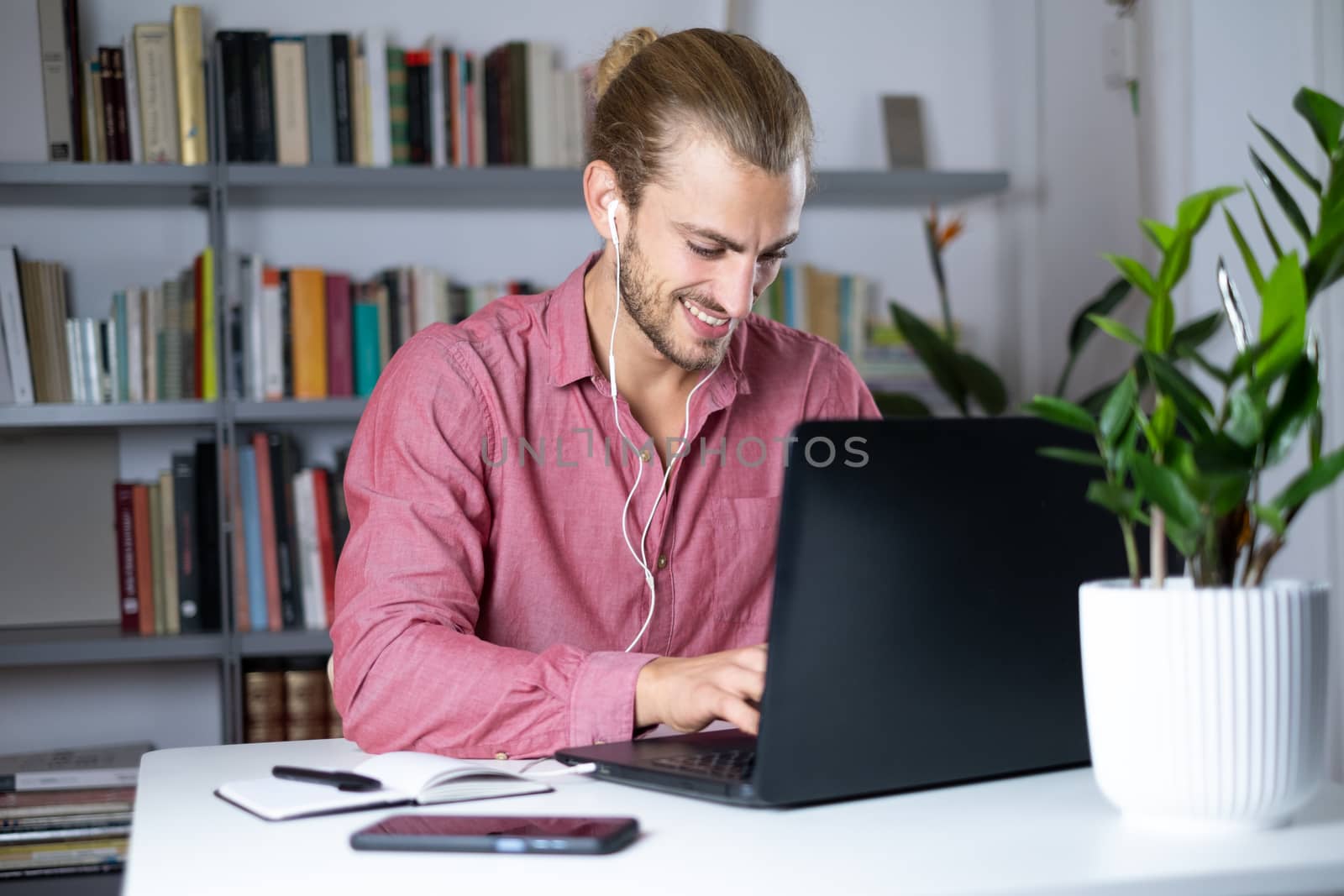 Attractive young man sitting at the table at home working with a laptop feeling happy
