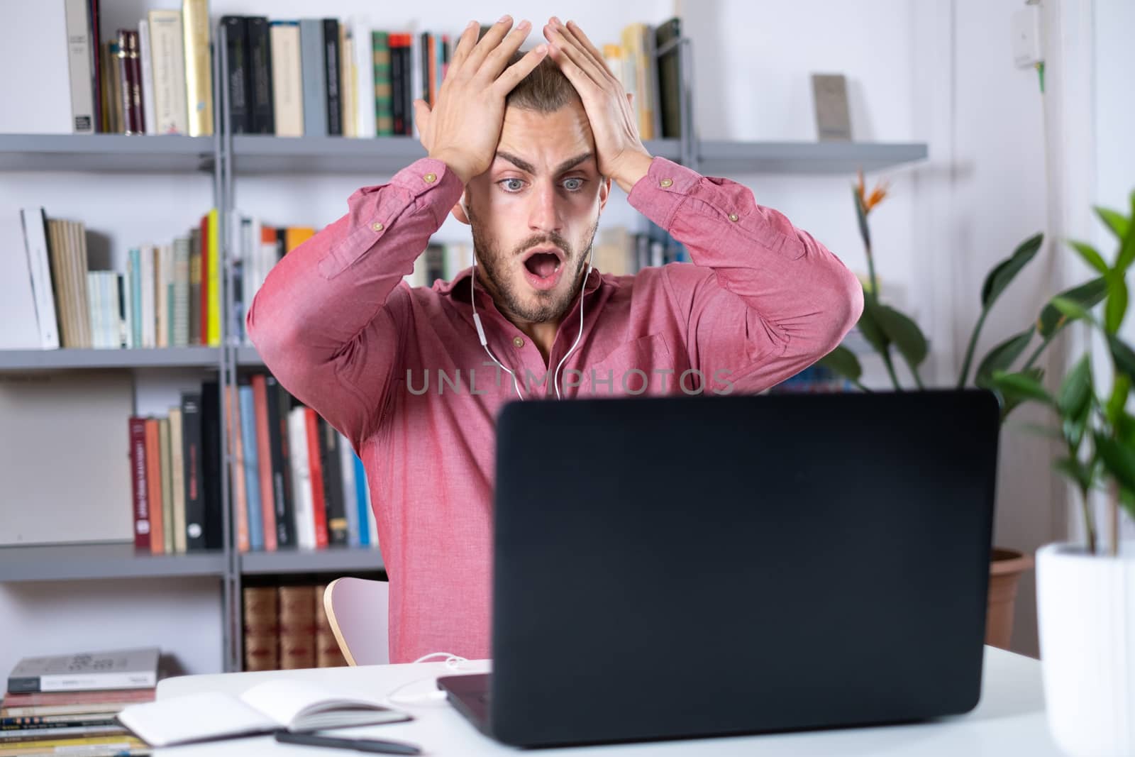 Attractive young man sitting at the table at home working with a laptop on a calling and feeling surprise